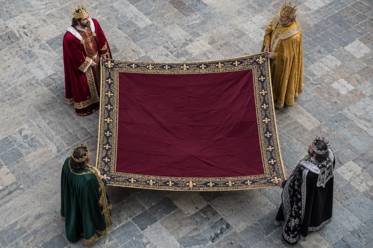 Four kings in costume, each standing at one corner of a large cloth laid on the paving.